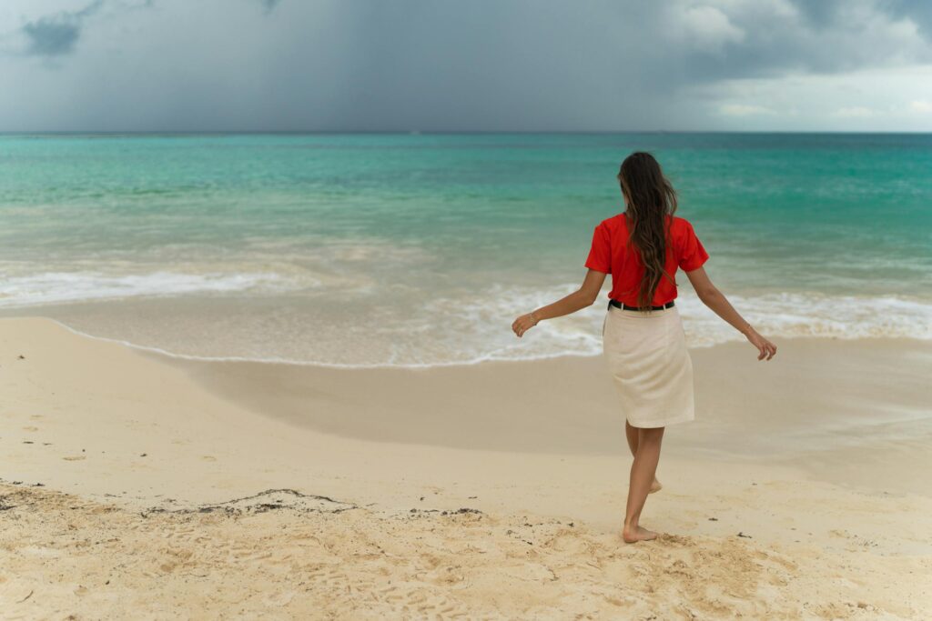 A woman strolls barefoot on Playa del Carmen's sandy shore under an approaching storm.